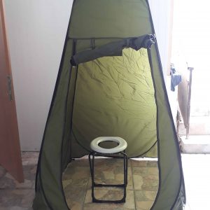 אוהל מקלחת חיצונית מתקפל אידיאלי כציוד קמפינג או לקרוואנים, מוצב ליד דלת פתוחה ומדרגות על פת קרמיקה – מתאים במיוחד לשימוש עם מערכות אנרגיה סולארית, תאורת LED סולארית ותחנות כוח פוטו-וולטאיות ניידות לטובת ייצור חשמל נקי ותשתיות אנרגיה מתחדשת בשטח.