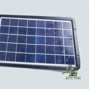 תקריב של פנס LED סולארי 15W 6000LM מלבני (פרוז'קטור לד סולארי) עם מסגרת שחורה, הכולל פאנלים פוטו-וולטאיים מתקדמים לייצור חשמל באנרגיה מתחדשת, על רקע בהיר; ציוד ידידותי לסביבה אידיאלי עבור קרוואנים (מוצרים לקרוואנים) או ציוד מחנאות (ציוד לקמפינג). לוגו קטן עם טקסט בעברית מופיע בפינה הימנית התחתונה, המדגיש פתרונות אנרגיה סולארית ברי קיימא ומחוץ לרשת.