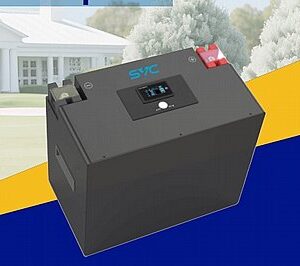 סוללת ליתיום SVC 12.8V 314Ah למערכות אנרגיה סולארית, עם תצוגה ומחברים, על משטח כחול-צהוב, בית ועצים ברקע.